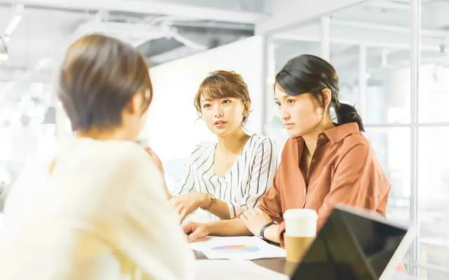 オフィスで資料を囲みながらミーティングする3名の女性
